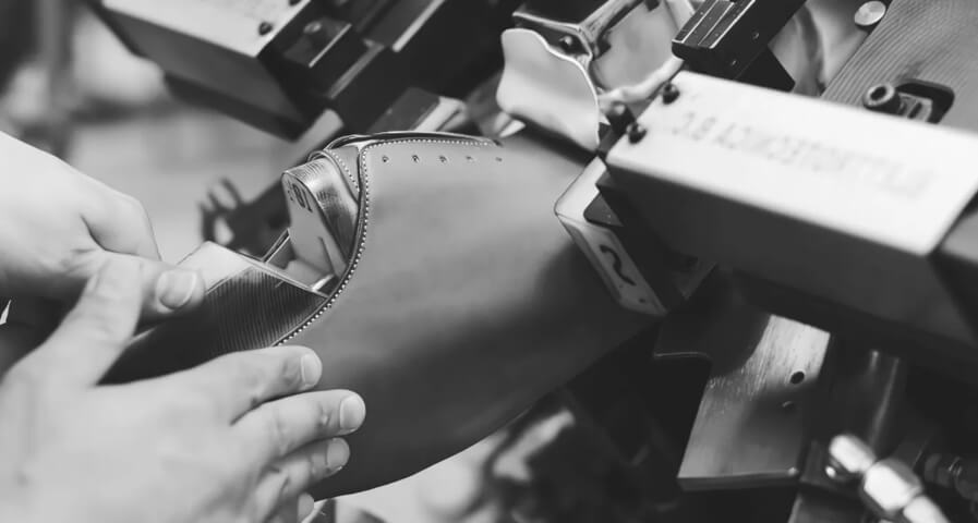 Shoemaker shaping a dress shoe with industrial equipment in a workshop
