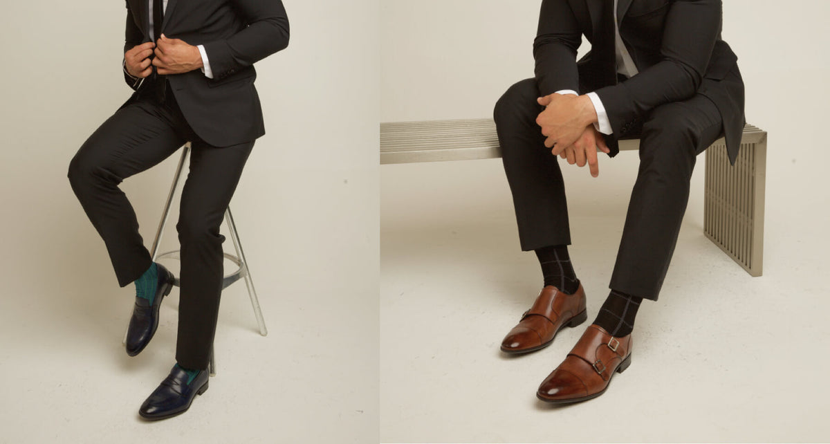 Man in a suit models dark blue dress shoes and brown monk strap shoes in a studio