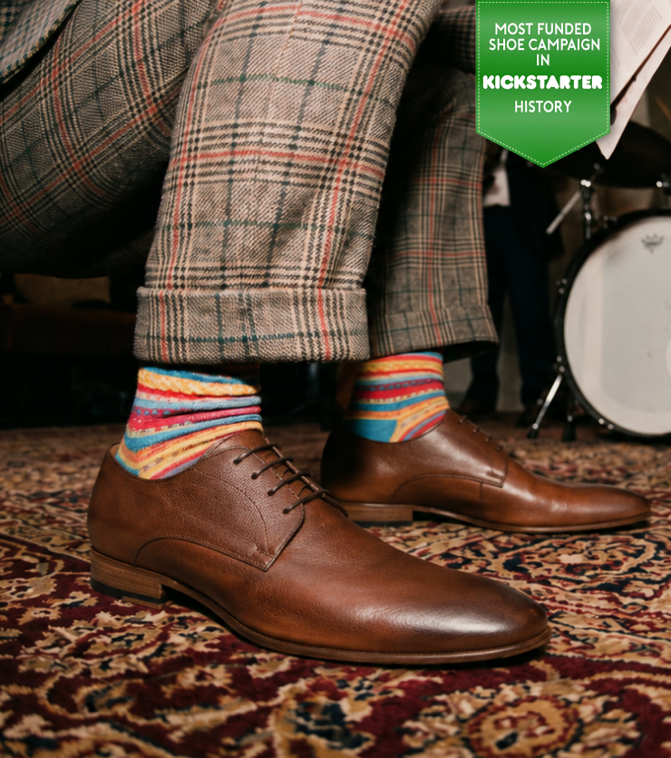 Man standing wearing men's brown Italian leather oxford dress shoes in a room with band equipment.