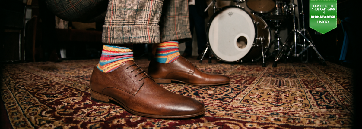 Man standing wearing men's brown Italian leather oxford dress shoes in a room with band equipment.