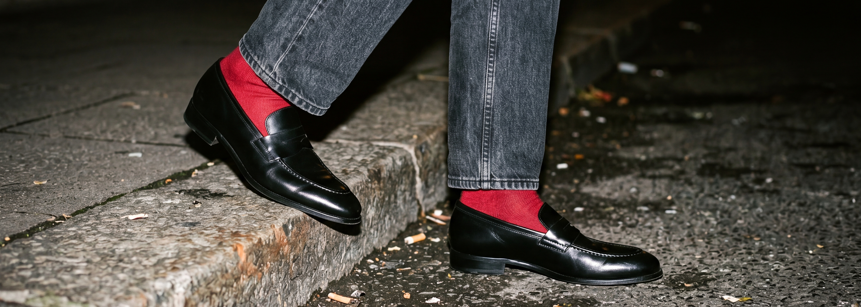 Man walking on street wearing jeans, red socks and men's Italian black leather penny loafer dress shoes.