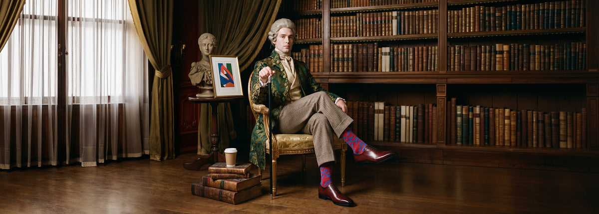 Victorian man sitting in library wearing men's brown Italian leather lace-up dress wholecut oxford shoes with brown plaid trousers and an ornate green and gold sports coat.